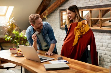Happy couple talking while shopping clothing online at home.