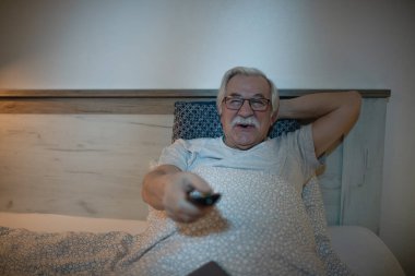 Mutlu olgun bir adam yatakta dinleniyor ve geceleri televizyon seyrediyor.. 