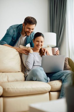 Happy woman and her husband surfing the net on laptop in the living room.
