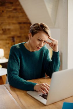 Pensive woman reading problematic e-mail on laptop at home. 