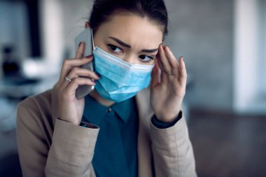 Distraught businesswoman talking over cell phone while working in the office during COID-19 pandemic.
