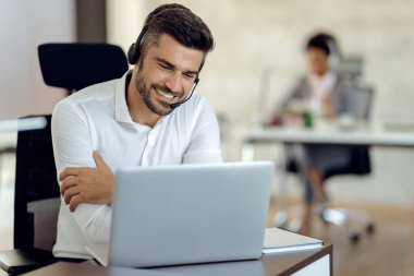 Young happy businessman wearing headset while using laptop in the office. 