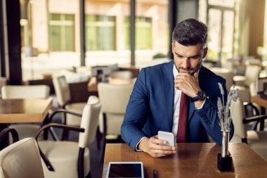 Businessman texting on smart phone while relaxing in a cafe. 