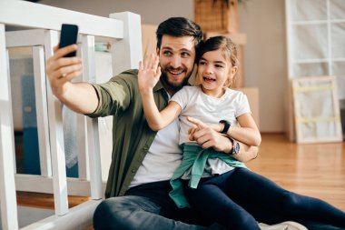 Happy little girl and her father having fun while taking selfie after moving into new home. 