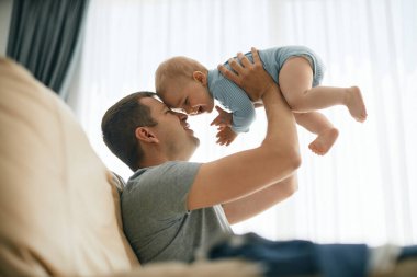 Happy father enjoying while playing with his baby son at home.