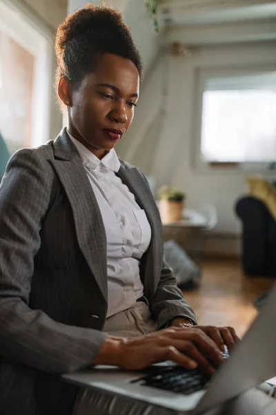 Black female entrepreneur typing on laptop while working at home office.