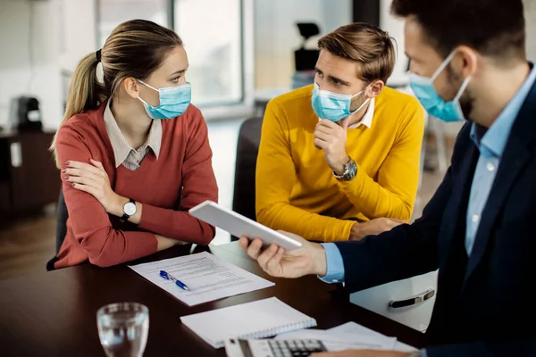 Young couple talking among themselves while having a meeting with financial advisor during coronavirus pandemic.