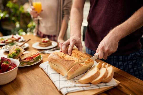 Close-up of man cutting loaf of bread during breakfast at home.