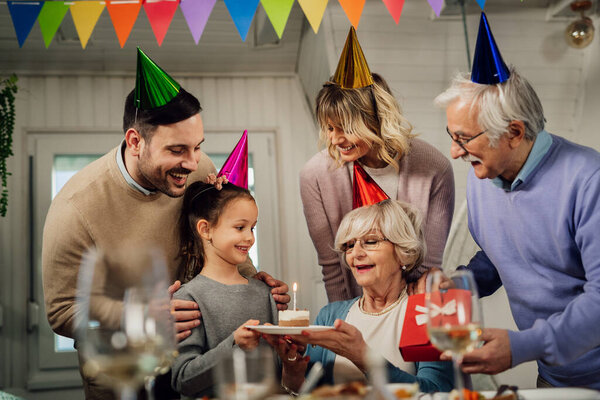 Happy multi-generation family having fun while celebrating grandmother's Birthday and surprising her with a cake. 