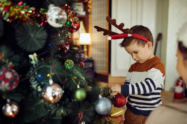 Small Boy Wearing Reindeer Antlers While Decorating Christmas Tree Home — Stock Photo, Image