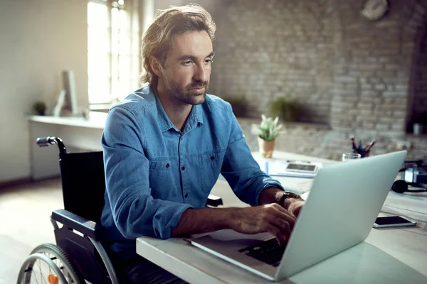 Young entrepreneur in wheelchair using computer while working in the office.