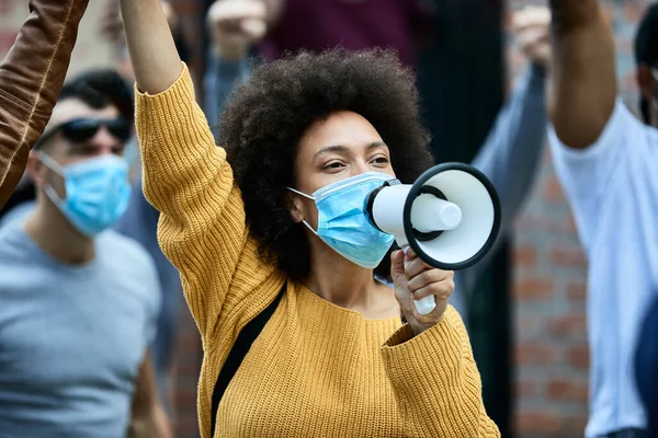 African American woman shouting through megaphone while wearing protective face mask on a anti-racism protest.