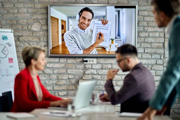 Happy entrepreneur joining a business meeting via video conference call and talking about paperwork with his colleagues.