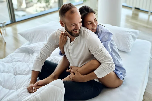 Young cheerful couple having fun while sitting embraced in the bedroom. 