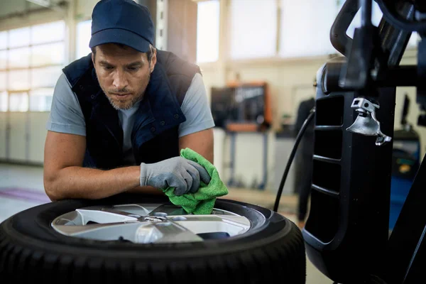 Distraught auto mechanic leaning on car tire and thinking while working in auto repair shop.