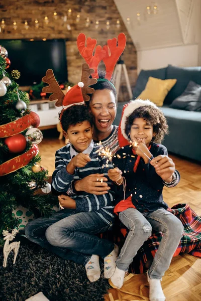 Joyful African American mother and her children having fun with sparklers while celebrating Christmas at home.