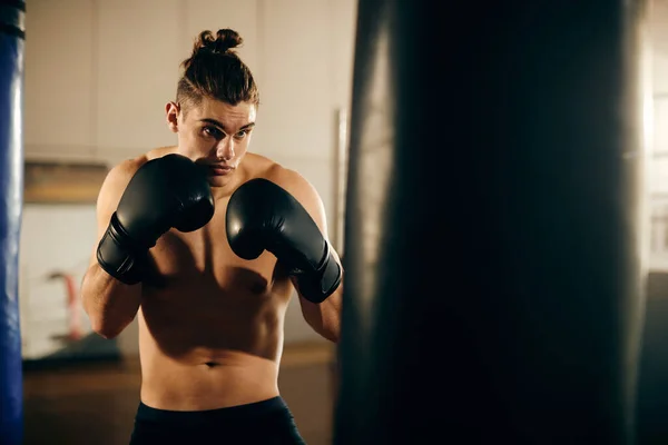 Muscular build boxer hitting punching bag while working out at boxing club.