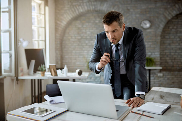 Mid adult entrepreneur surfing the net on a computer while working in the office. 
