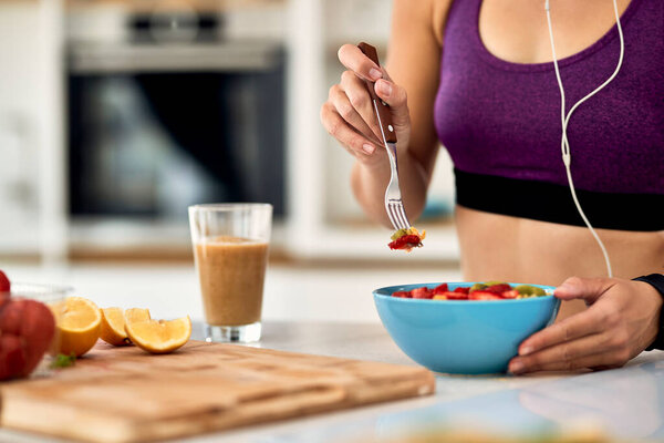 Close-up of female athlete having fruit salad for a snack in the kitchen. 