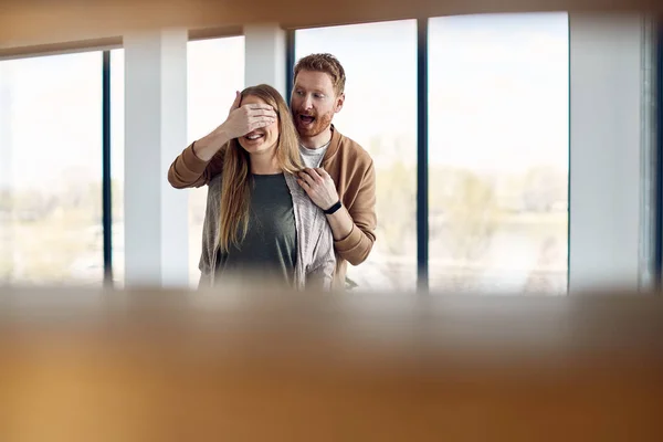 Young man covering wife\'s eyes while surprising her with their new home. Copy space.