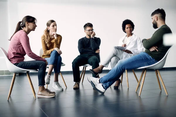 African American psychotherapist and attenders of group therapy sitting in a circle and communicating. Copy space.
