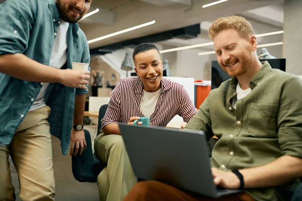 Group of happy entrepreneurs surfing the net on laptop during their coffee break in the office. Focus is on African American woman.