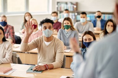 African American student raising his hand to answer a question while attending lecture in the classroom during COVID-19 pandemic. 