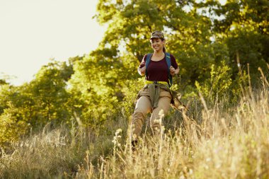 Low angle view of happy woman with backpack walking down the hill while hiking in nature.