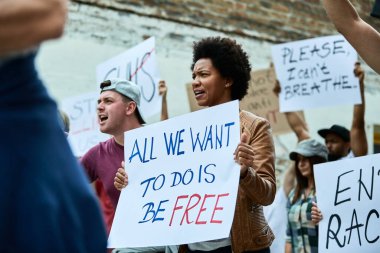 Crowd of people demonstrating against race-related discrimination. Focus is on woman carrying banner with freedom inscription. 