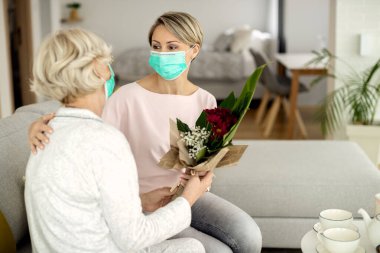 Adult daughter bringing bouquet of flowers to her mother while vising her during coronavirus epidemic. 