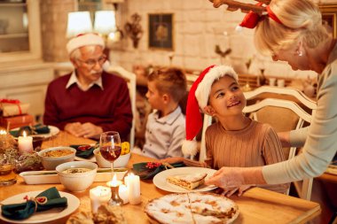 Happy little girl talking to her grandmother while she is serving her apple pie during family lunch on Christmas day.