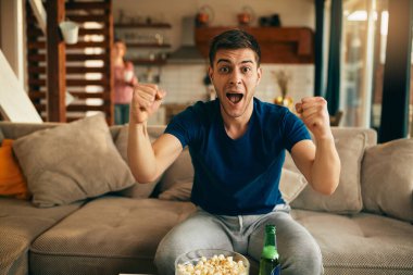 Young man cheering for his favorite team while watching sports match on TV at home. 