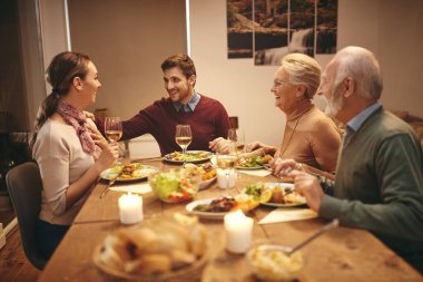 Happy man talking to his wife while they are having dinner with his senior parents at dining table. 