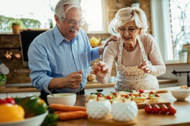 Happy senior couple enjoying while preparing healthy food together in the kitchen. 