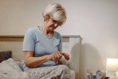 Mature woman taking a pill while sitting on the bed at night. 