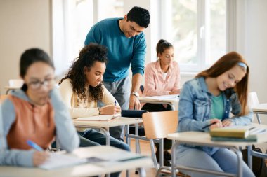 African American high school student leaning with teacher's help in the classroom.