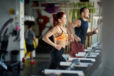 Dedicated athletes jogging on treadmills while warming up for sports training in a gym.  Focus is on woman. 