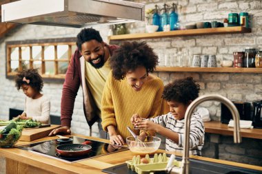 Happy black parents and their kids making a meal together in the kitchen. 