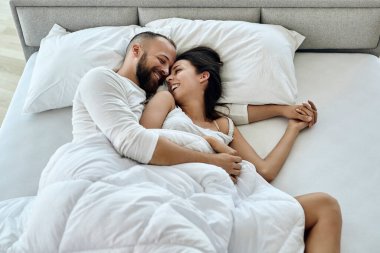 High angle view of happy couple having fun while waking up together in the morning. 