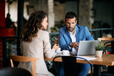 Businessman and his female colleague talking while working on a computer in a cafe. 