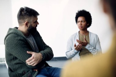 Black woman talking about her problems while meeting with support group  at psychotherapy in medical center. 