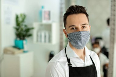 Portrait of hairdresser wearing protective face mask while working at hair studio during coronavirus epidemic. 