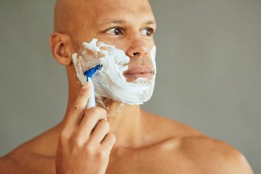 Afrika kökenli Amerikalı bir adamın tıraş olurken jilet kullanması ve bakışlarını kaçırması..