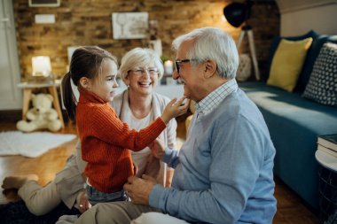 Happy senior couple enjoying with their granddaughter at home. 