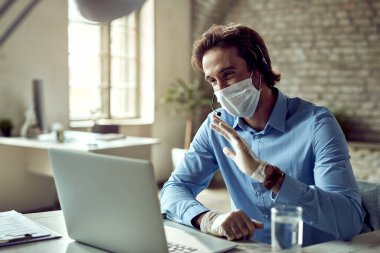 Happy businessman waving while having online meeting over laptop during COVID-19 pandemic. 