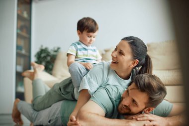 Young parent having fun while making human pyramid with their son at home.