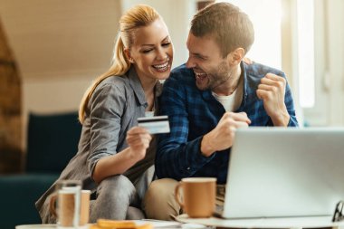 Happy couple having fun and celebrating while using credit card for e-banking at home. 