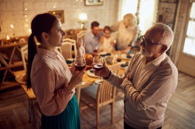 Mid adult woman and her mature father celebrating Thanksgiving with their family and drinking wine while talking in dining room.