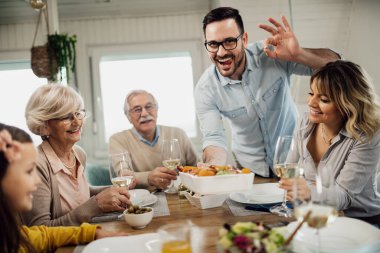 Happy man serving lunch to his family and showing OK sign while looking at camera. 