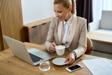 Happy businesswoman surfing the net on a computer while drinking coffee in hotel room. 